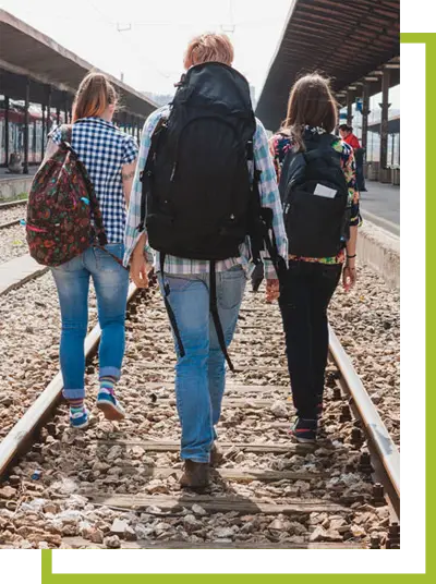 Tres jóvenes con mochilas caminando sobre vías del tren.